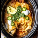 Slow cooker chicken enchiladas topped with avocado slices, jalapeños, cilantro, and sour cream.