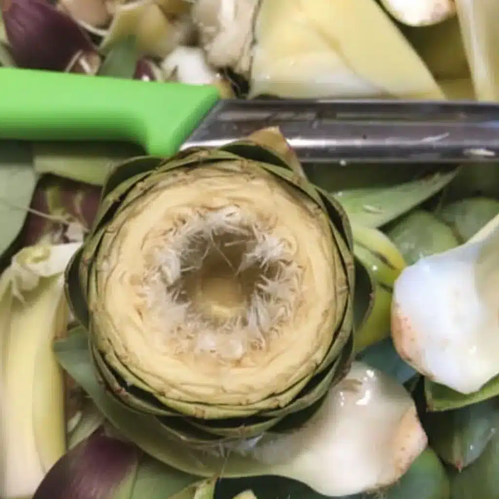 Stuffed Artichoke Bottoms Made Easy with One Great Recipe 10 Artichoke heart with choke being cleaned for stuffed artichoke bottoms.